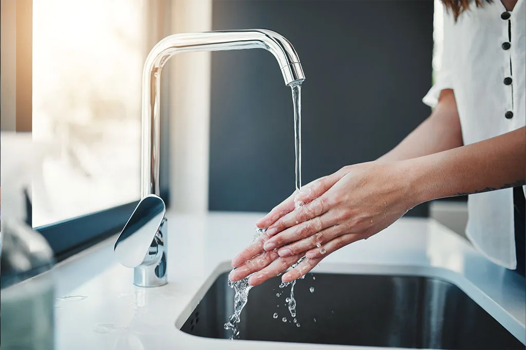 Hände werden unter fließendem Wasser aus dem Hahn gewaschen
